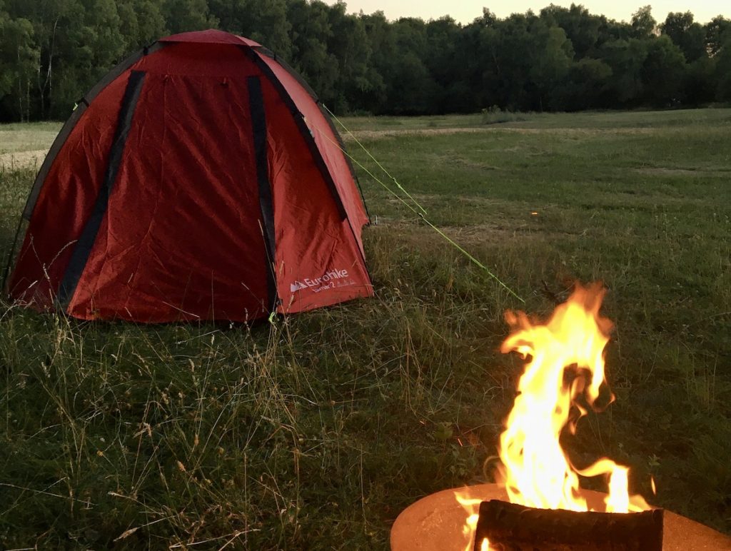 A red tent in a field with a campfire in the foreground