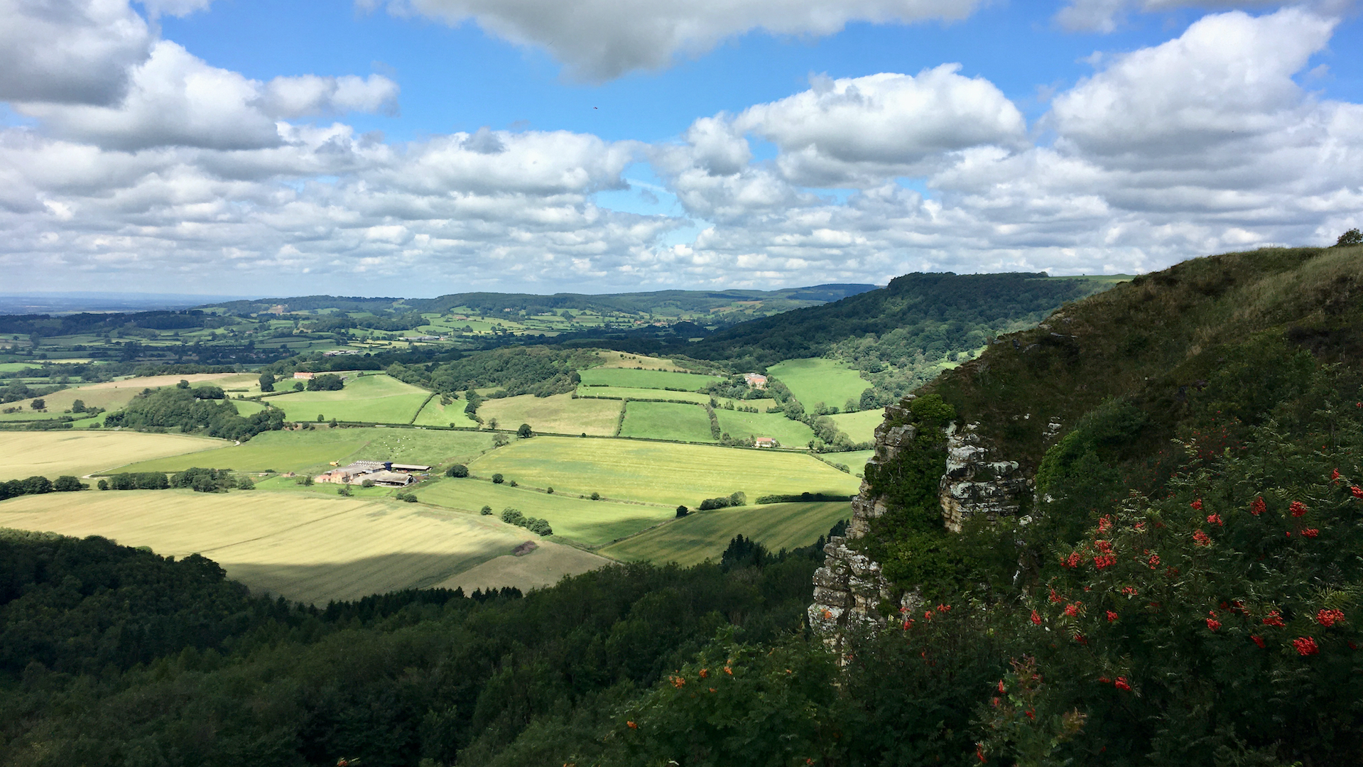 A landscape with rocks in the shade in the foreground, with a patchwork of green fields in the background. The type of view you may see on our navigation courses or workshops.