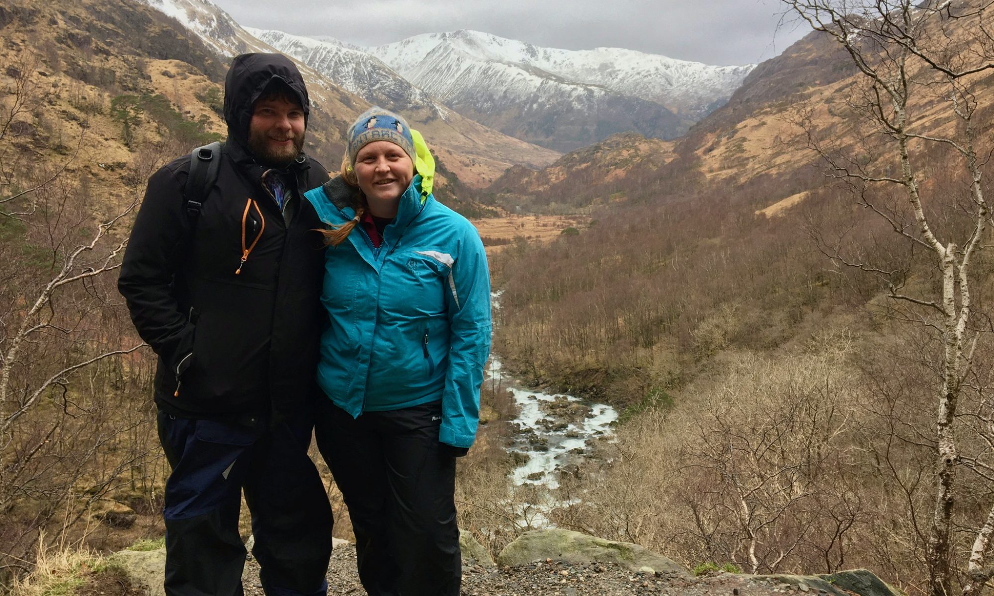 Two people dressed in full waterproofs stood in front of a snowy mountain view